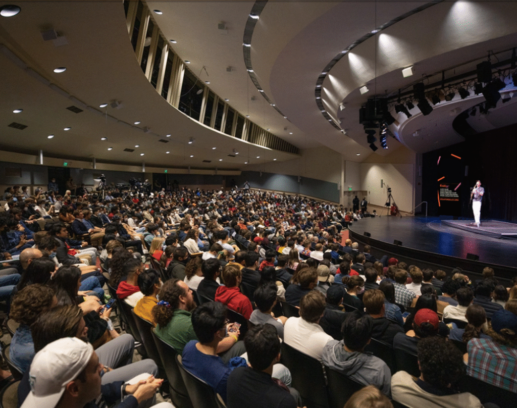 A single speaker on a stage speaking to a full auditorium of people.